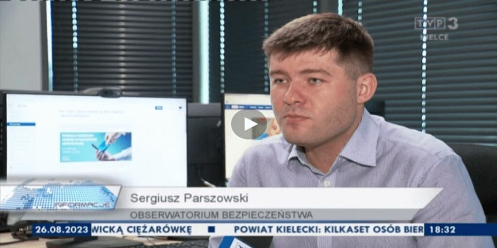 Sergiusz Parszowski udzielający komentarza dla TVP Kielce. W tle stanowiska komputerowe.