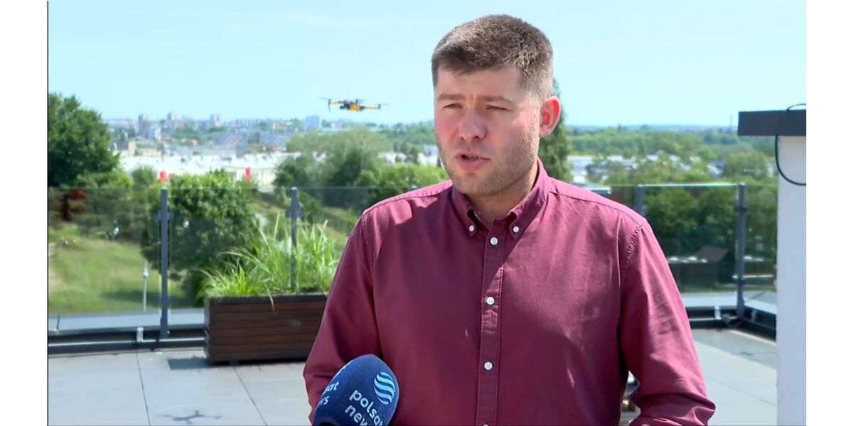 Kadr z programu Polsat News. Sergiusz Parszowski w bordowej koszuli stojący na zewnątrz mówi do mikrofonu, który trzyma niewidoczna druga osoba. W tle krajobraz miejski: dachy budynków i drzewa. Na niebie lecący dron.