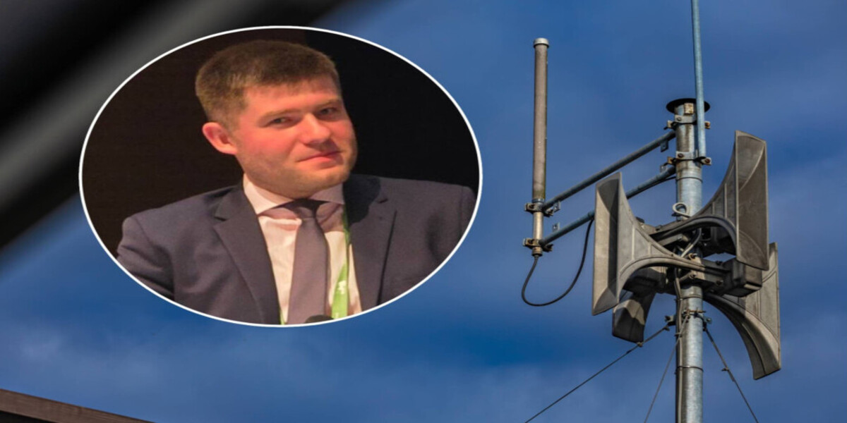 Fotomontaż przedstawiający w okrągłym wcięciu po lewej stronie portret młodego mężczyzny w ciemnym garniturze i krawacie, na tle zdjęcia syreny alarmowej umieszczonej na słupie pod błękitnym niebem.