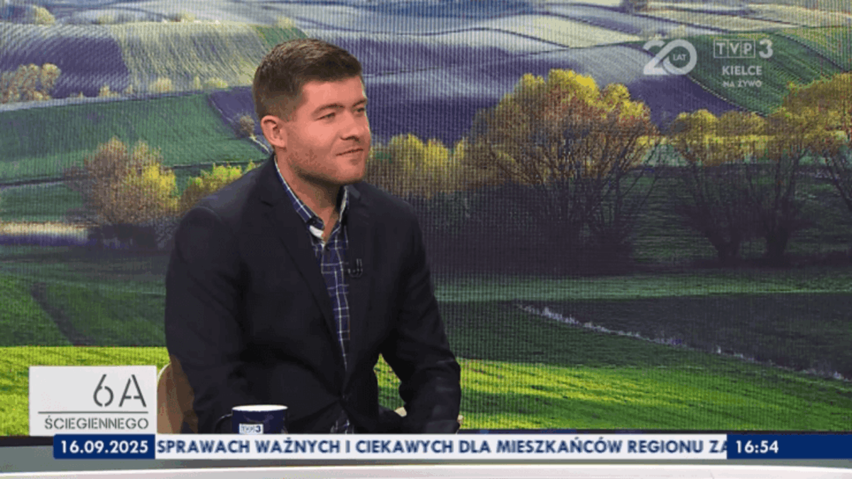 Mężczyzna siedzi na krześle, ubrany w marynarkę i koszulę w kratę. Znajduje się w telewizyjnym studiu, w tle widoczny jest krajobraz z polami i drzewami. Na ekranie widnieją loga i napisy TVP3 Kielce.