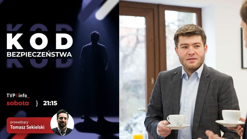 Mężczyzna w szarym garniturze trzyma filiżankę kawy. Obok niego po lewej stronie znajduje się plakat z napisem 